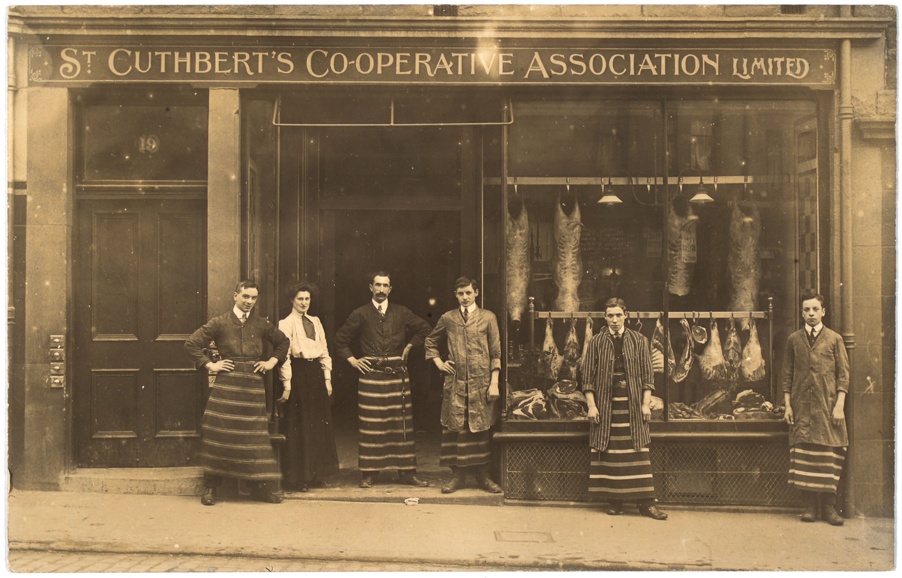 A group of people standing outside a butchers shop in the 1900s