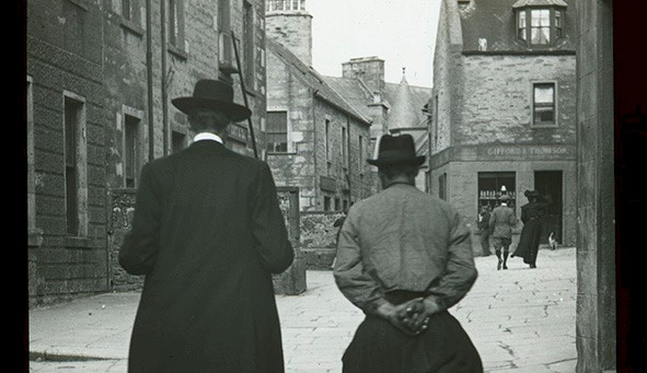 A black and white photo with two men walking through a street 