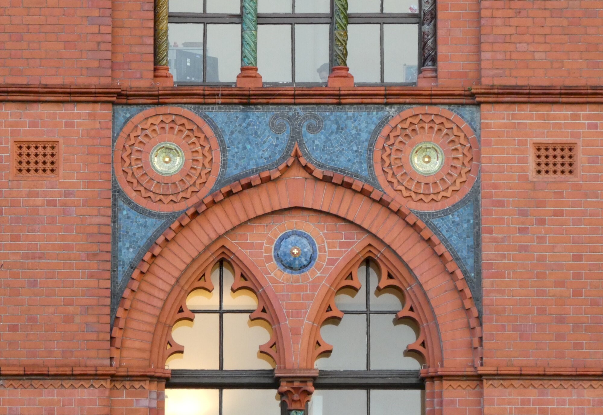 An ornate sequence of red and blue tiles on the outside wall of a building, with windows above and below.