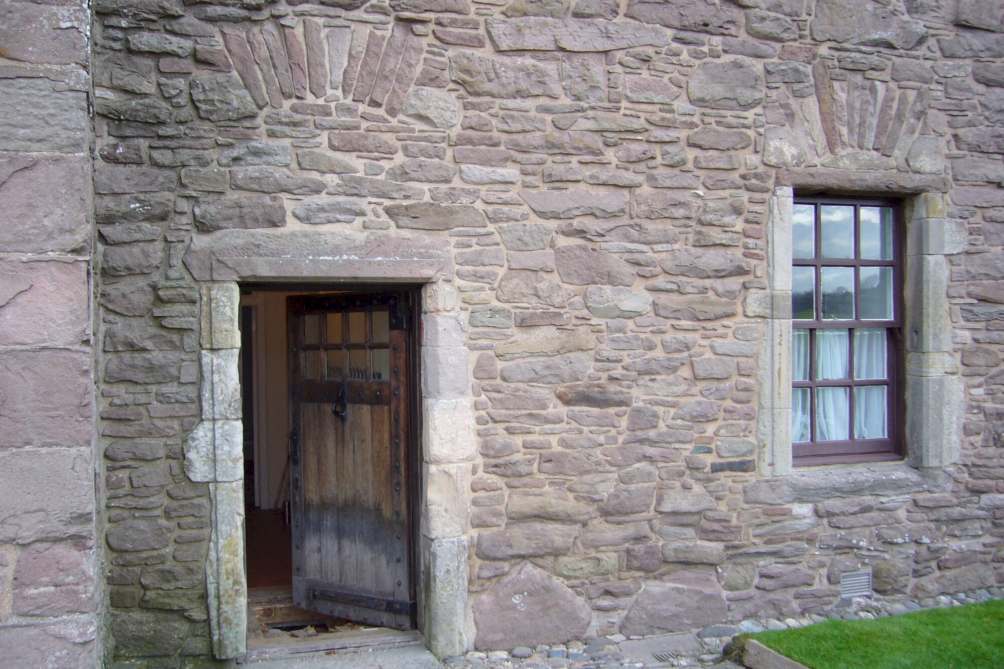 A timber door and window set into the side of a historic castle wall, made up of many intricate stones and shaped bricks.