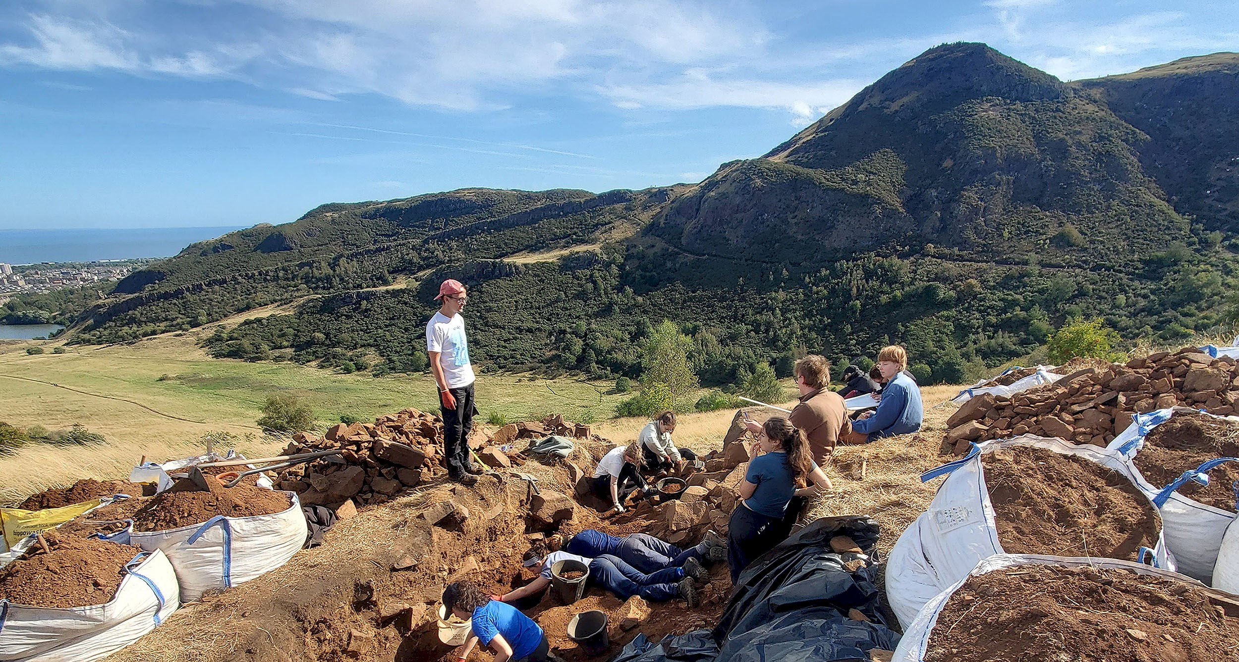 People doing an archaeological dig with beautiful blue sky and green hills